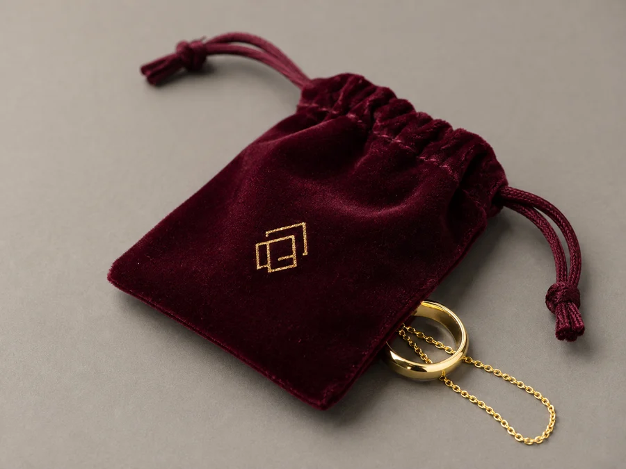 Burgundy velvet drawstring pouch with gold foil monogram and a gold ring and chain